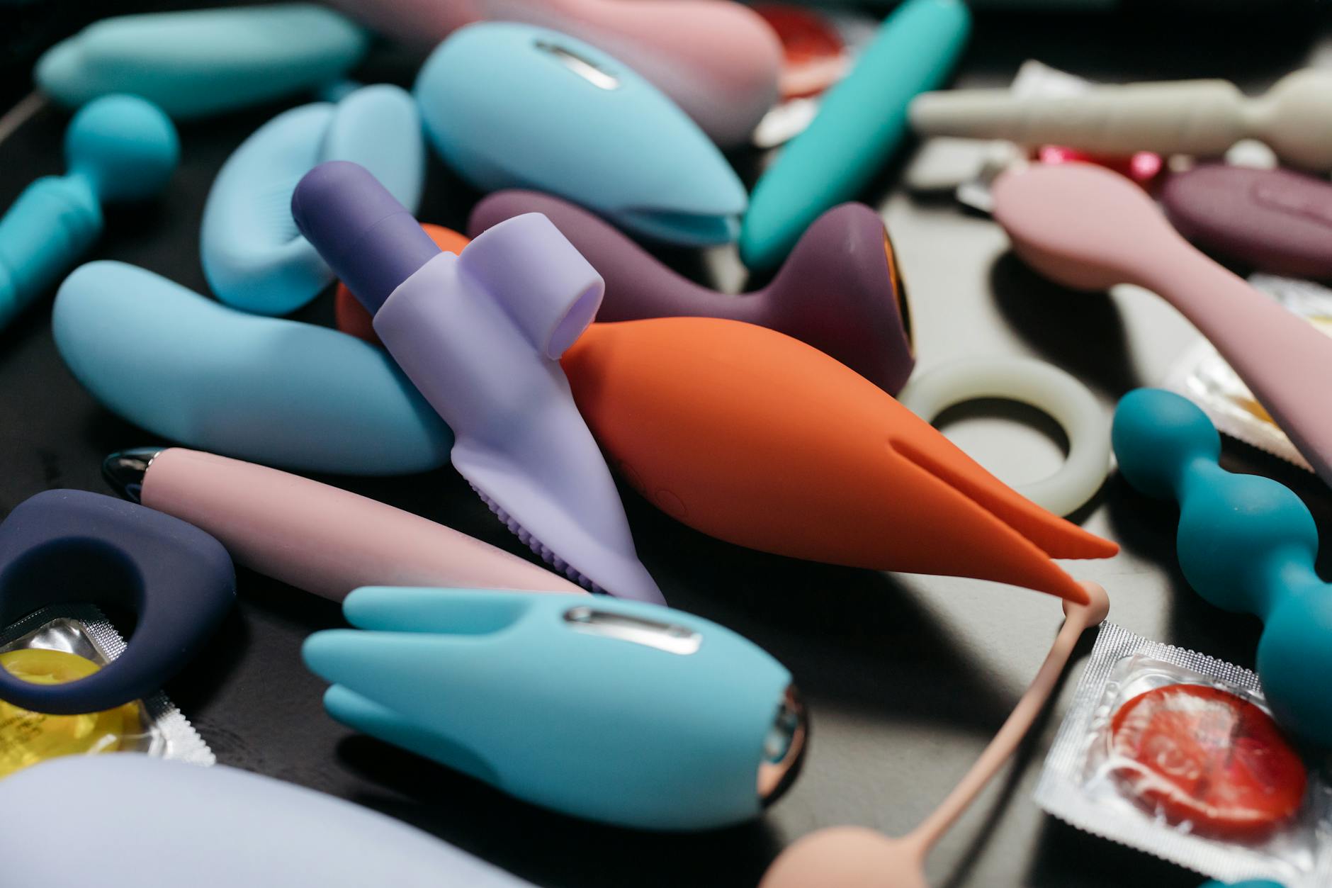 A young woman with eyeglasses holds two colorful vibrators against a purple background