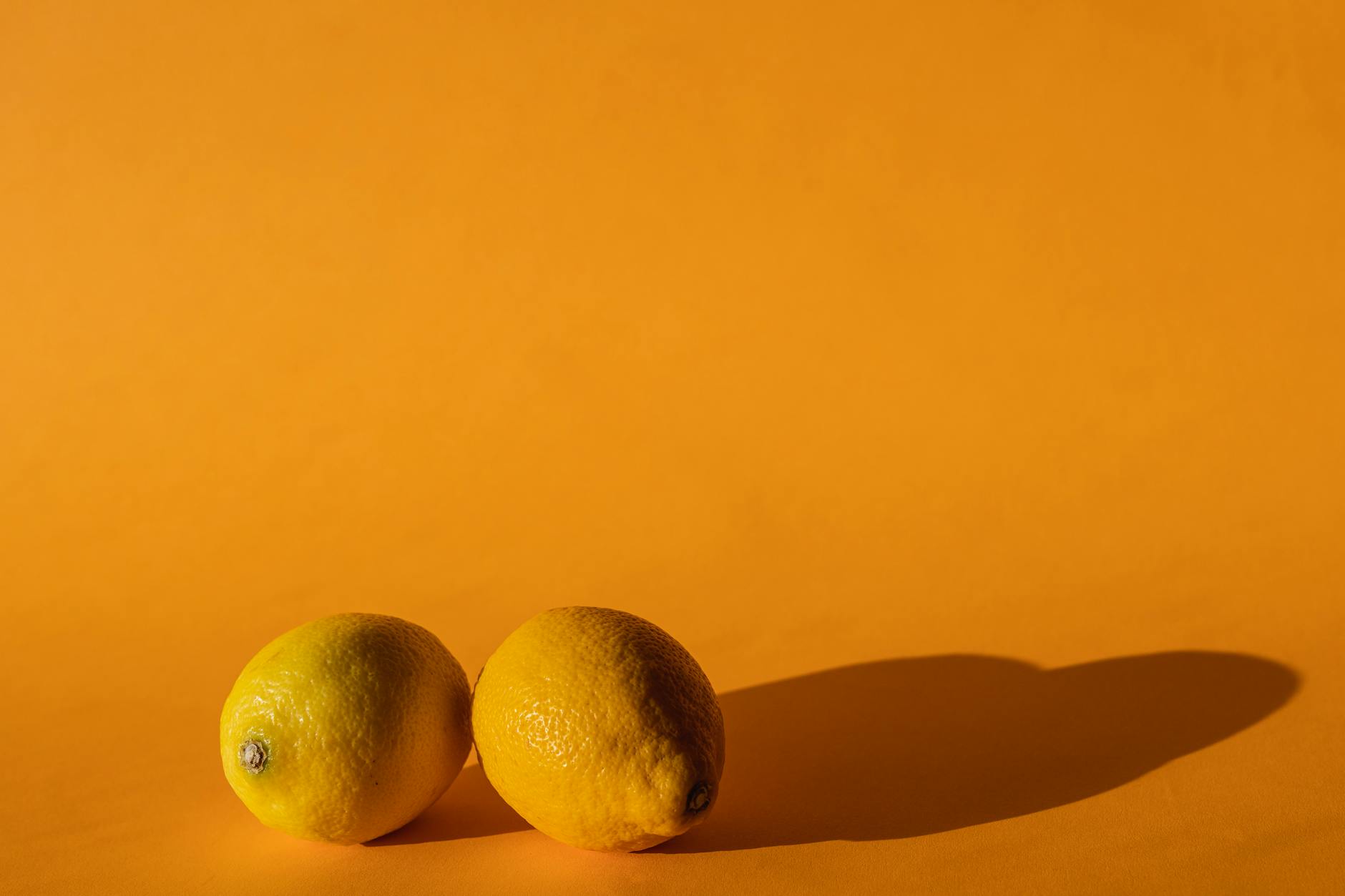 A hand holding a sleek lemon clitoral vibrator against a minimalistic purple backdrop